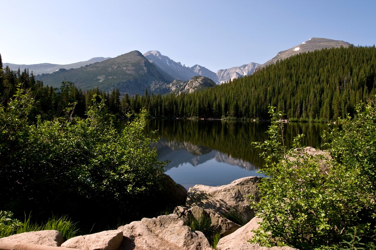 An alpine lake reflects the surrounding peaks on a sunny summer day in Rocky Mountain National Park in Colorado.