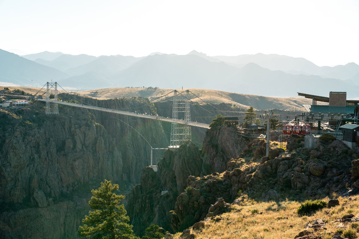 A valley of trees under the Royal Gorge Bridge in Cañon City. In the background is a landscape of faded blue mountains against the skyline.