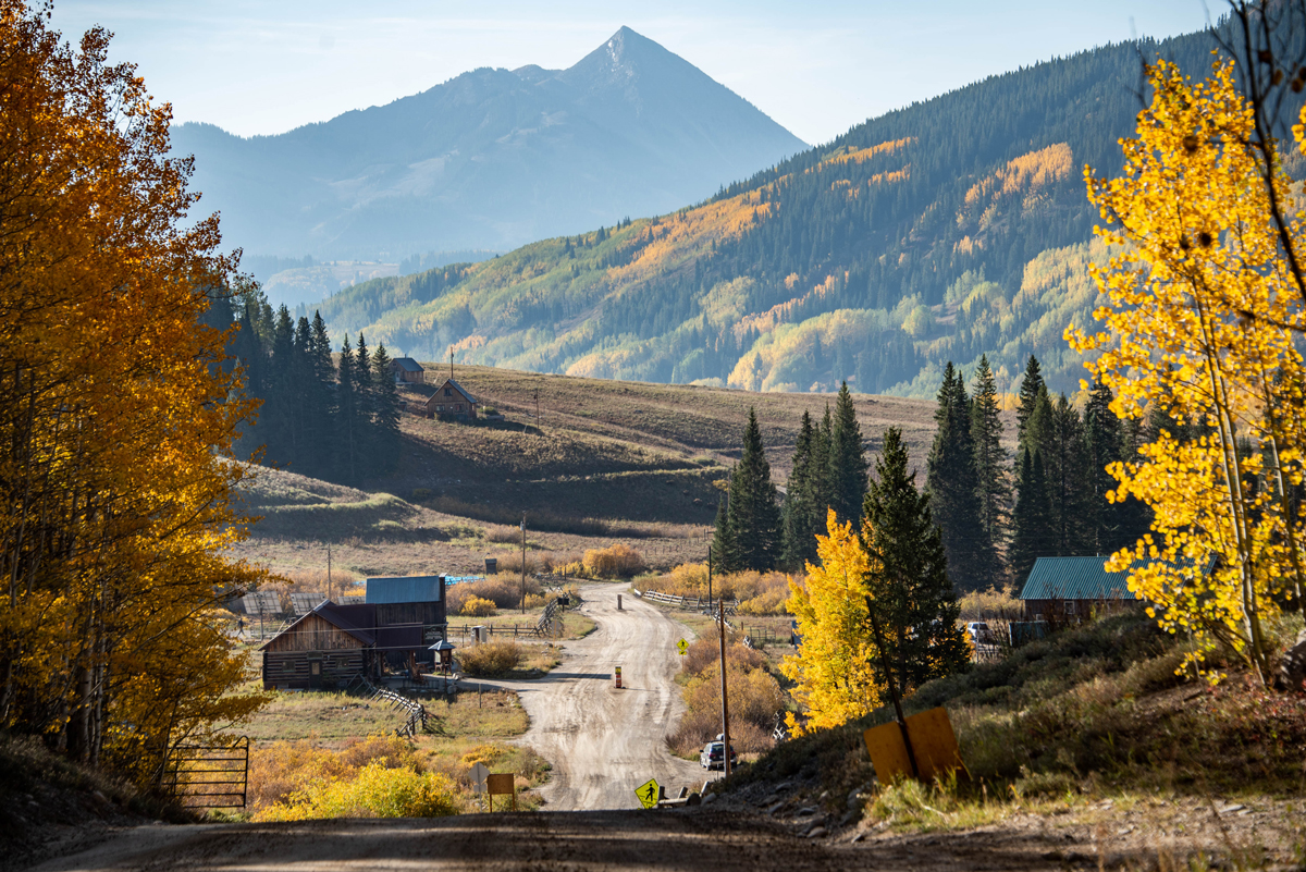 A dirt road cuts through a small town of historical old west buildings surrounded by golden aspens in Gothic, Colorado. 