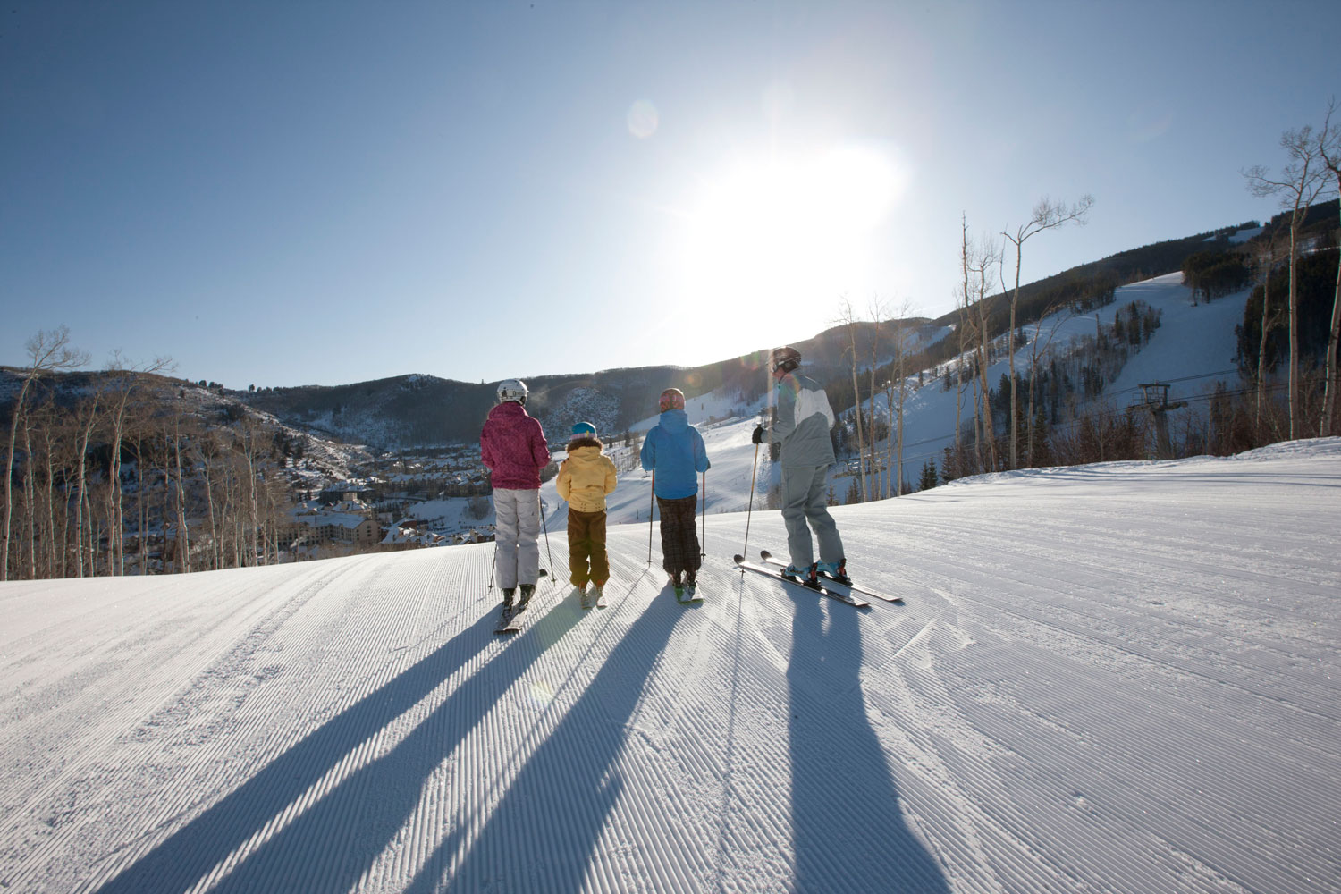 Four skiers look out onto the town of Avon's ski run with fresh, corduroy snow beneath their skis.