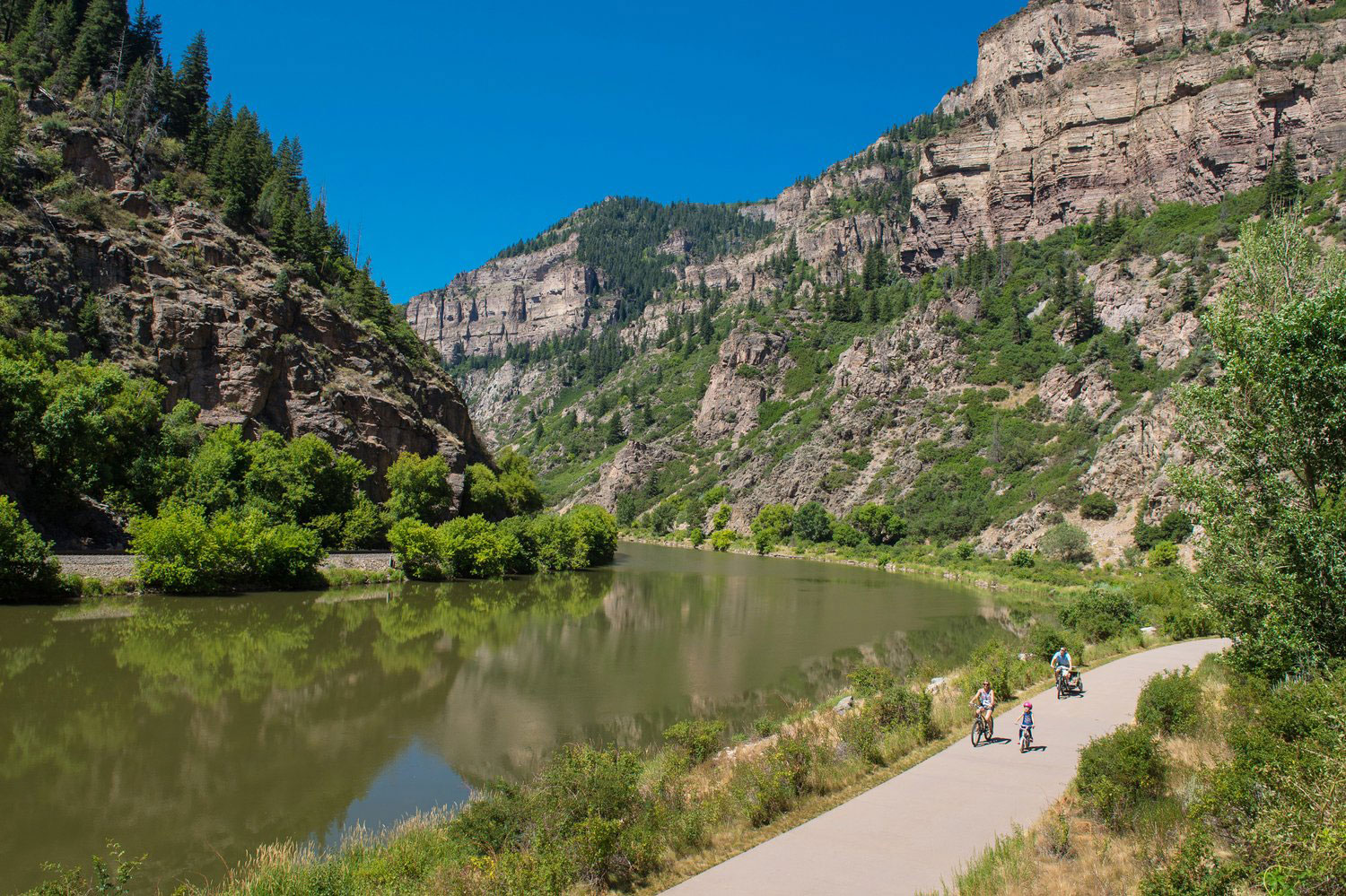 Family bike riding alongside a body of water in Glenwood Canyon