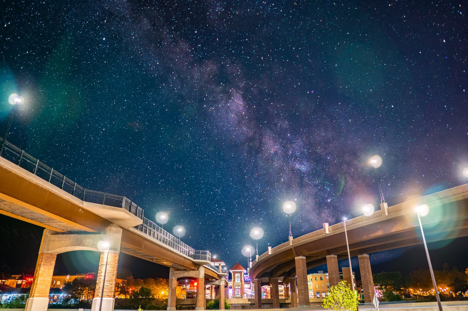 Two bridges wind near each other and from the angle below, seem to frame the night sky in Glenwood Springs, Colorado. Above, hundreds of stars twinkle and a purple, cosmic cloud colors the sky.