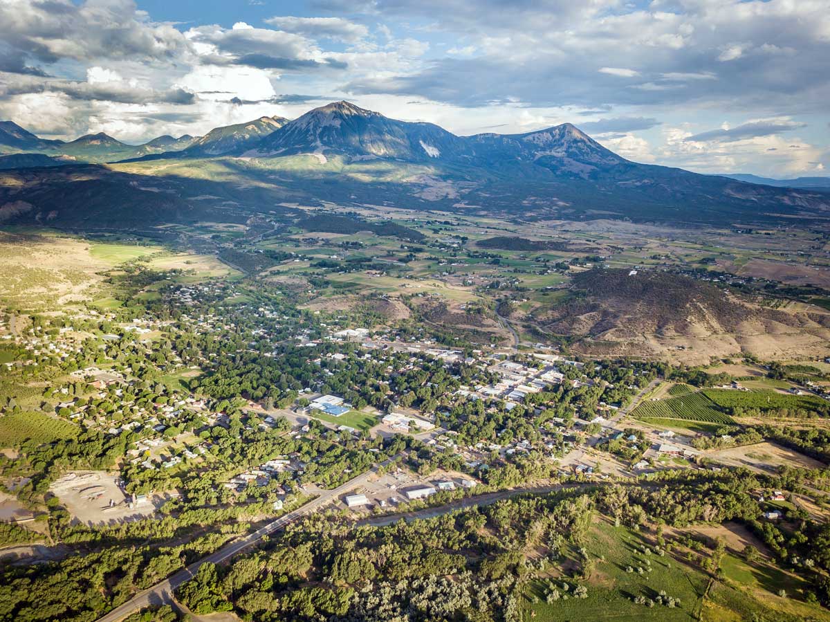An aerial view of summer in Paonia. The town is nestled in a valley with green trees and mountains in the background.