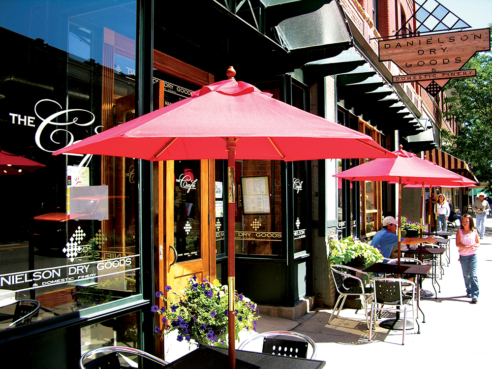 Tables under red umbrellas line a street with cafes and potted planters