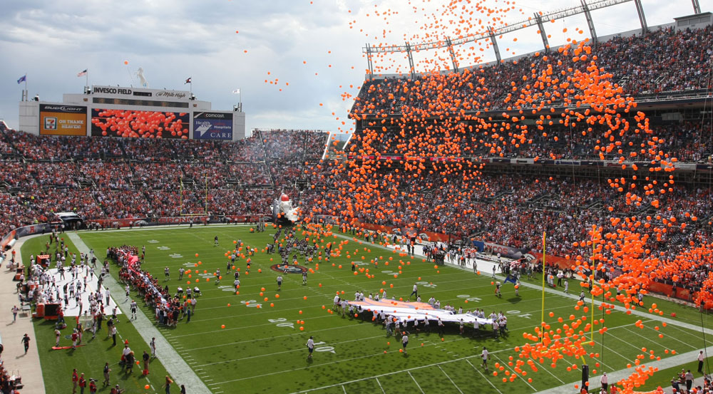 Orange balloons float over the green football field and a packed stadium of Broncos fans in Denver, Colorado.