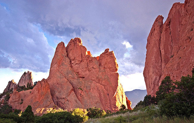 The red sandstone formations jut from the ground at the Garden of the Gods in Colorado Springs. The sun shines on the backs of the formations during sunset.