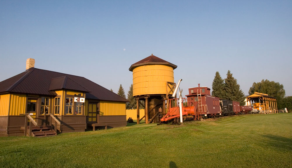A station house and water tower are painted bright yellow, and a caboose is sitting on nearby tracks