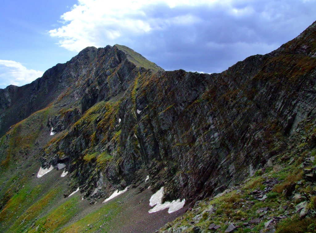 A rugged mountain ridge, part of the Venable-Comanche Trail, is covered in patches of moss and lichen near Westcliffe, CO. They sky above is moody with a patch of sun breaking through dark clouds.