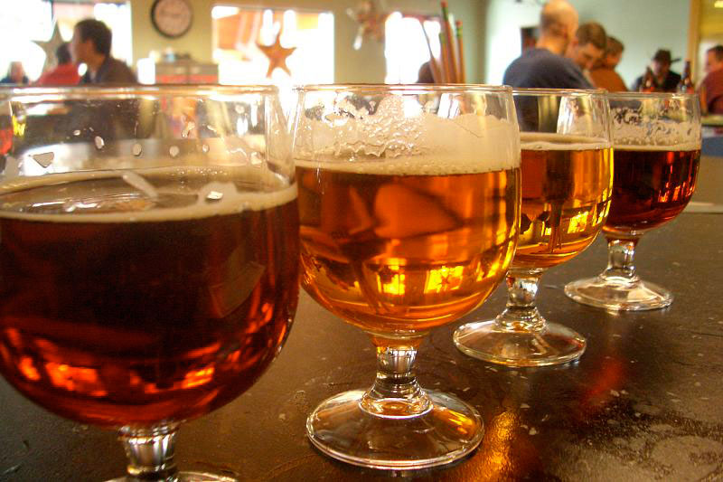 Four stemmed beer glasses stand side by side on a bar counter in Fort Collins, Colorado. Each holds amber-colored beer with a rim of froth near the top.